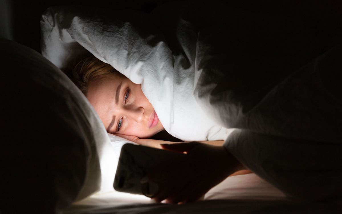 Using ChatGPT as therapy late at night Woman awake in bed at night, her face lit only by her phone